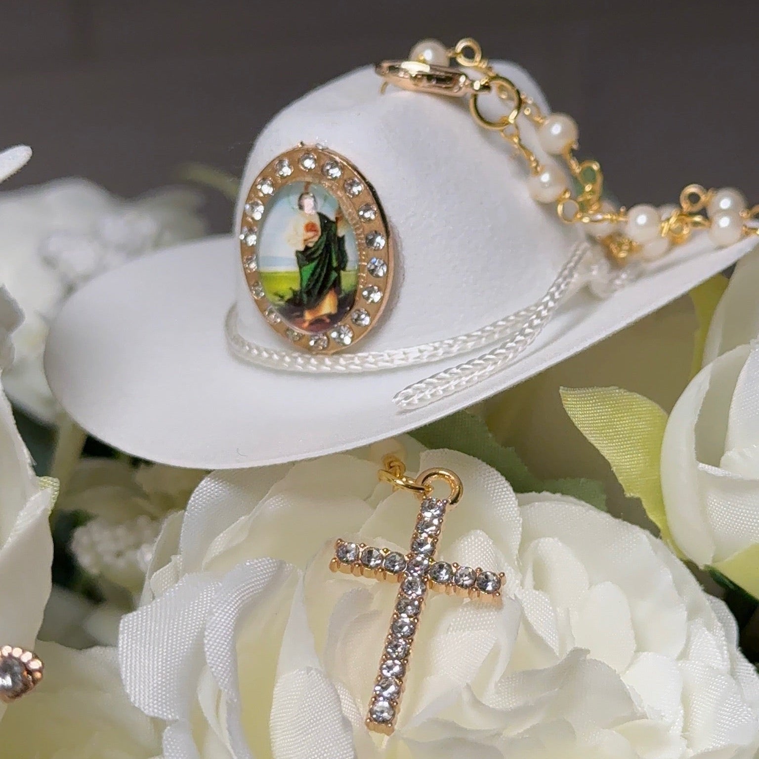 White hat with religious emblem and cross pendant on white flowers